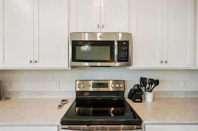 kitchen with stainless steel appliances, white cabinets, and light stone counters