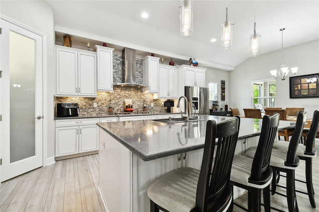 kitchen with pendant lighting, white cabinetry, a kitchen island with sink, stainless steel appliances, and wall chimney range hood