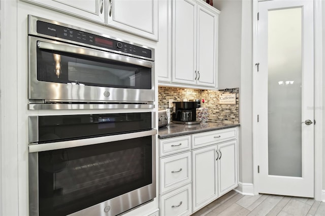 kitchen featuring tasteful backsplash, light wood-type flooring, white cabinets, and double oven