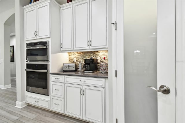 kitchen with white cabinetry, tasteful backsplash, stainless steel double oven, and light hardwood / wood-style flooring