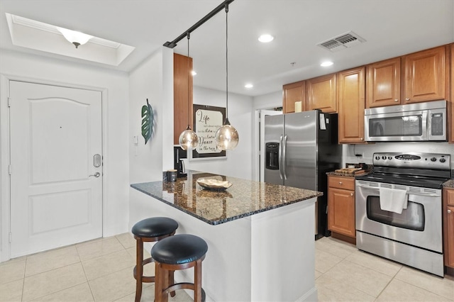 kitchen with light tile patterned flooring, appliances with stainless steel finishes, decorative light fixtures, a kitchen breakfast bar, and dark stone counters