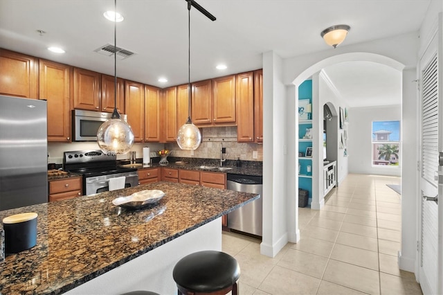 kitchen with dark stone counters, stainless steel appliances, pendant lighting, sink, and backsplash