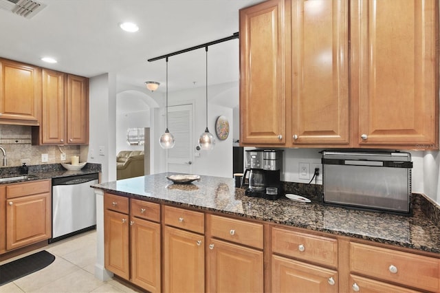 kitchen with dark stone countertops, hanging light fixtures, stainless steel dishwasher, and sink