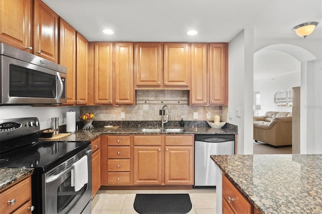 kitchen with appliances with stainless steel finishes, tasteful backsplash, dark stone countertops, sink, and light tile patterned flooring