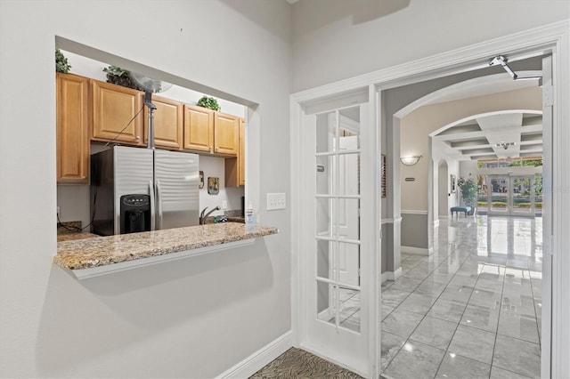 kitchen featuring light tile patterned flooring, stainless steel fridge with ice dispenser, beamed ceiling, coffered ceiling, and light stone counters