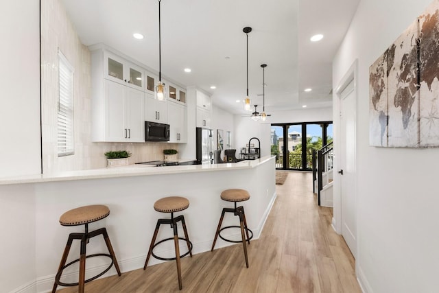 kitchen with a breakfast bar, white cabinetry, light wood-type flooring, black microwave, and stainless steel refrigerator