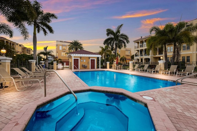 pool at dusk with a patio area and a hot tub