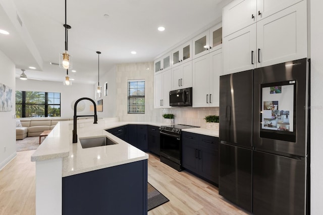 kitchen featuring light stone counters, a peninsula, a sink, white cabinets, and black appliances