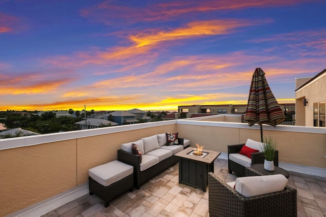 patio terrace at dusk featuring a balcony and an outdoor living space with a fire pit