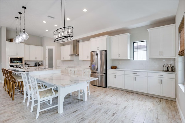 kitchen featuring stainless steel refrigerator with ice dispenser, wall chimney exhaust hood, built in microwave, a kitchen island with sink, and white cabinets