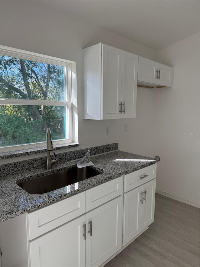 kitchen featuring white cabinetry, sink, dark stone counters, and light hardwood / wood-style flooring