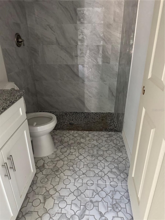 bathroom featuring a tile shower, vanity, and toilet