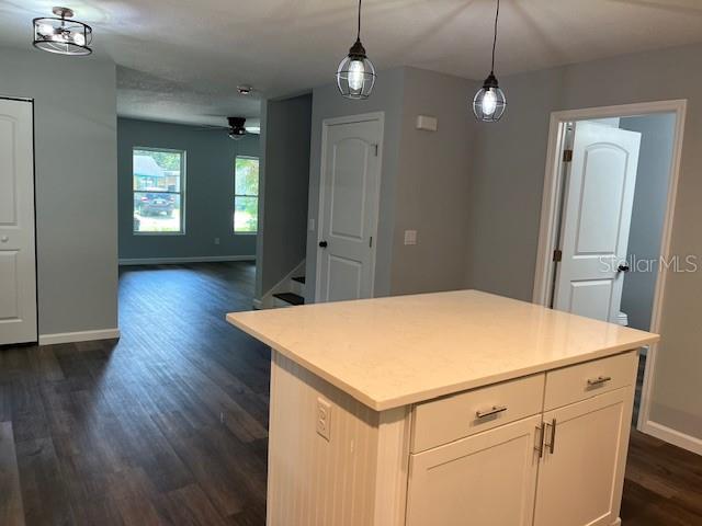 kitchen with dark wood-type flooring, hanging light fixtures, a kitchen island, white cabinetry, and ceiling fan