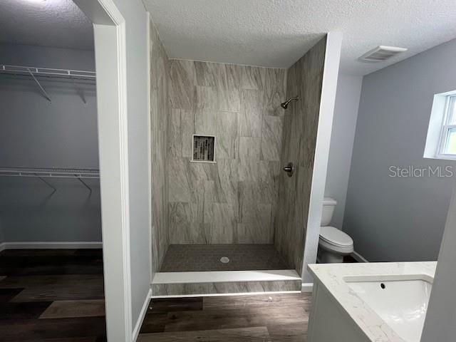 bathroom with toilet, a tile shower, vanity, and a textured ceiling