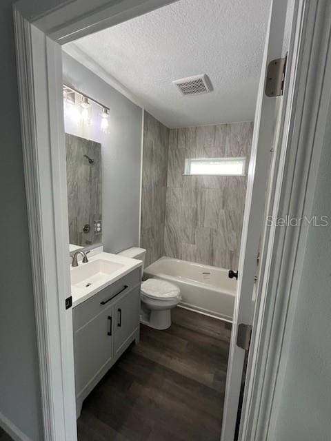 full bathroom with hardwood / wood-style floors, toilet, vanity, tiled shower / bath, and a textured ceiling