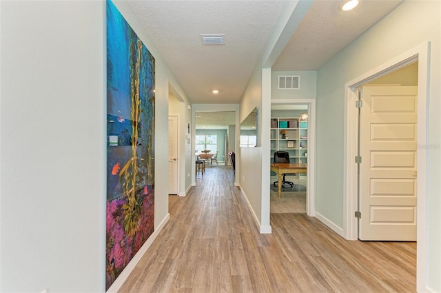 hall with light hardwood / wood-style flooring and a textured ceiling