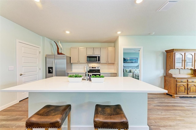 kitchen with light hardwood / wood-style floors, appliances with stainless steel finishes, a breakfast bar area, and an island with sink