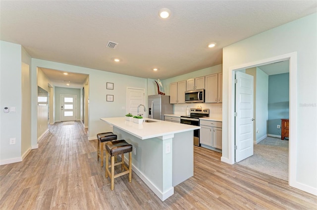 kitchen with stainless steel appliances, sink, a kitchen bar, light hardwood / wood-style flooring, and a kitchen island with sink