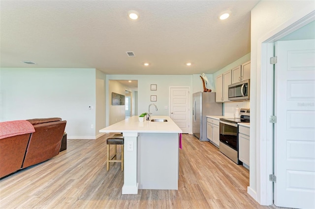 kitchen with sink, appliances with stainless steel finishes, an island with sink, and light wood-type flooring