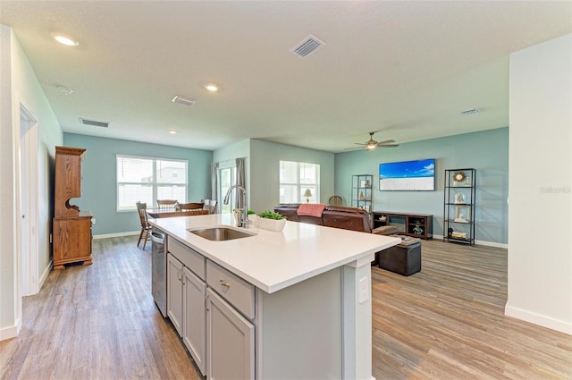 kitchen featuring stainless steel dishwasher, gray cabinets, an island with sink, light hardwood / wood-style floors, and sink