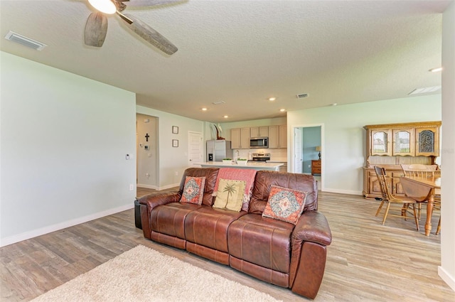 living room with a textured ceiling, ceiling fan, and light wood-type flooring