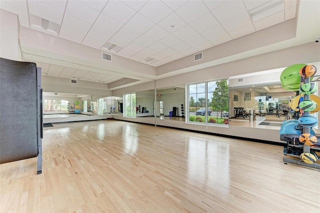 exercise room featuring light hardwood / wood-style floors, a drop ceiling, and a tray ceiling