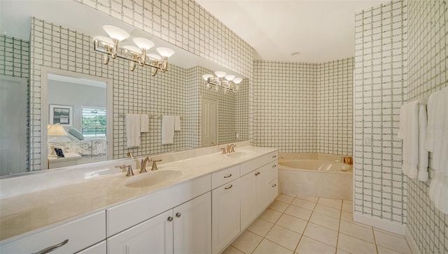 bathroom with tile walls, dual vanity, a tub to relax in, an inviting chandelier, and tile patterned flooring