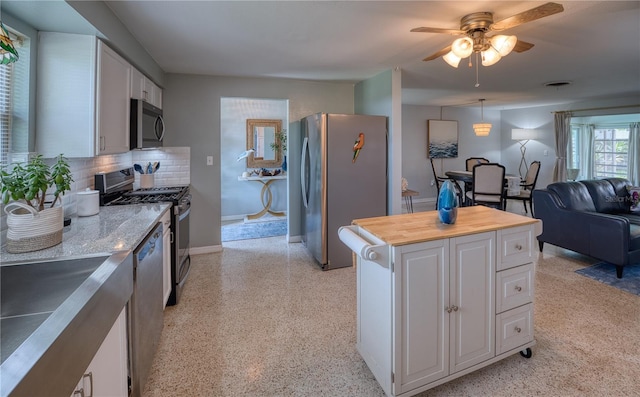 kitchen featuring stainless steel appliances, backsplash, decorative light fixtures, white cabinetry, and ceiling fan