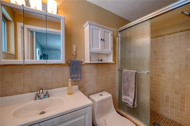 bathroom with a shower with shower door, vanity, tile walls, and toilet