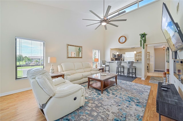 living room with light hardwood / wood-style flooring, ceiling fan, and a high ceiling