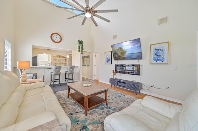 living room featuring ceiling fan, wood-type flooring, and a towering ceiling