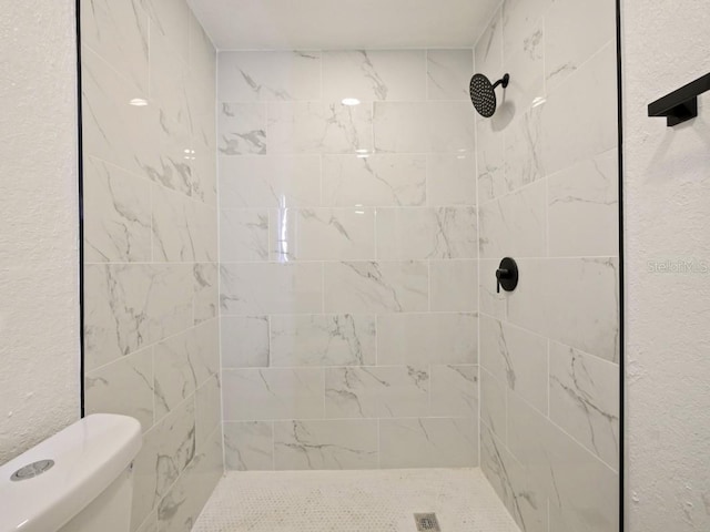 bathroom with a tile shower and toilet