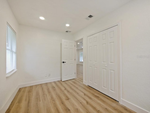 unfurnished bedroom with multiple windows, a closet, and light hardwood / wood-style flooring