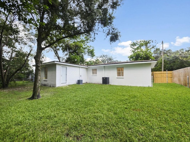 back of property with central AC unit and a yard