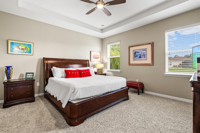 bedroom featuring light carpet, a tray ceiling, baseboards, and a ceiling fan