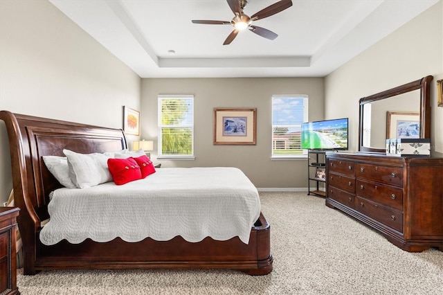 bedroom featuring a ceiling fan, a tray ceiling, light carpet, and baseboards