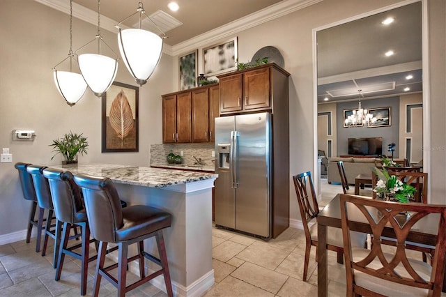 kitchen with stainless steel fridge with ice dispenser, hanging light fixtures, light stone countertops, brown cabinetry, and crown molding