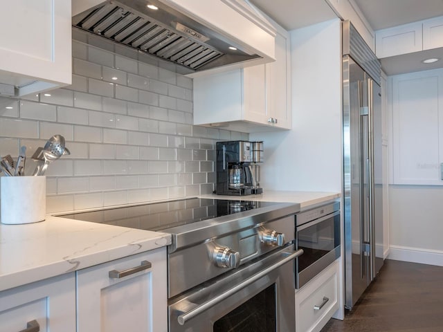 kitchen featuring white cabinetry, high quality appliances, custom range hood, light stone countertops, and backsplash