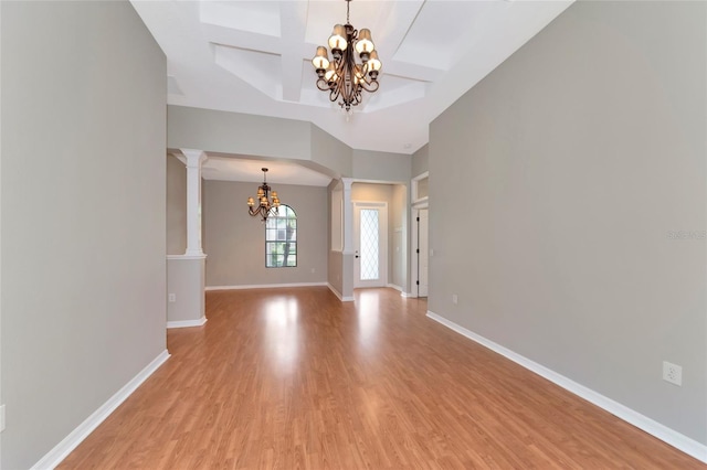 spare room with a notable chandelier, ornate columns, wood-type flooring, and coffered ceiling