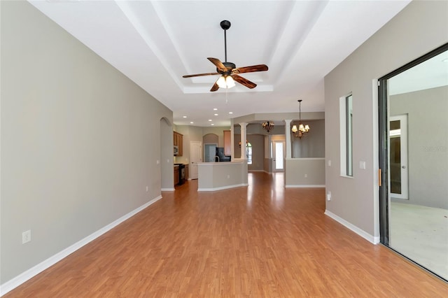 unfurnished living room featuring ceiling fan with notable chandelier, light wood-type flooring, and a tray ceiling