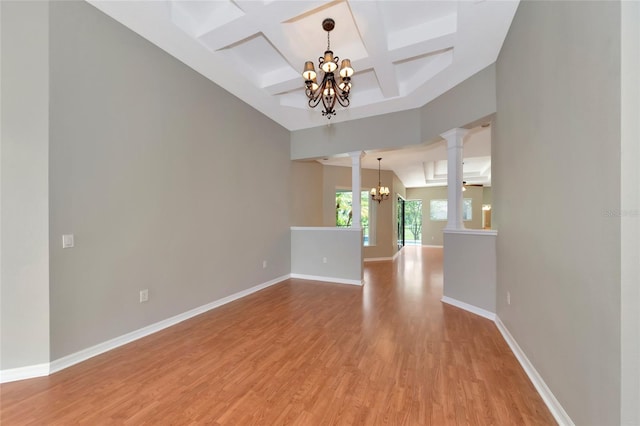 spare room with beamed ceiling, light hardwood / wood-style flooring, an inviting chandelier, ornate columns, and coffered ceiling