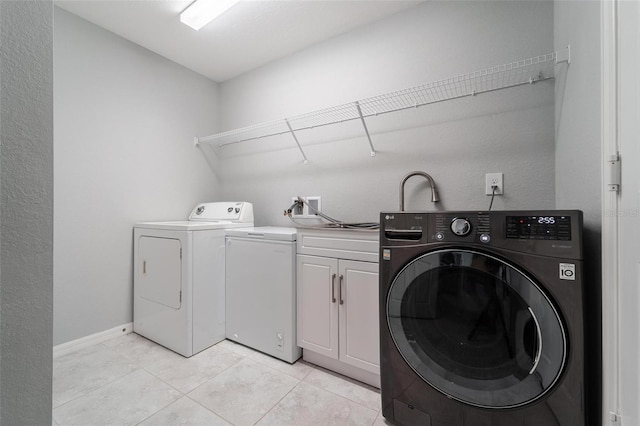 clothes washing area featuring light tile patterned floors, washer and clothes dryer, and cabinets