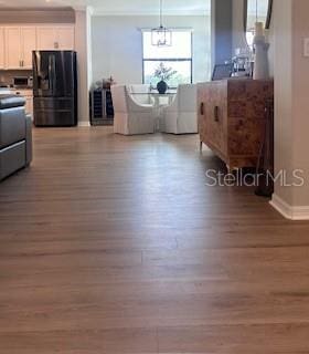 kitchen with white cabinets, black refrigerator, hanging light fixtures, light hardwood / wood-style flooring, and stainless steel range