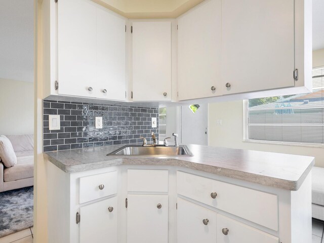 kitchen featuring light tile patterned floors, kitchen peninsula, white cabinets, backsplash, and sink