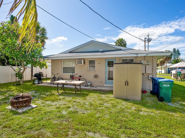 rear view of property featuring a patio area, a wall mounted air conditioner, a yard, and an outdoor fire pit