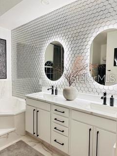 bathroom with dual vanity, decorative backsplash, and a bathtub