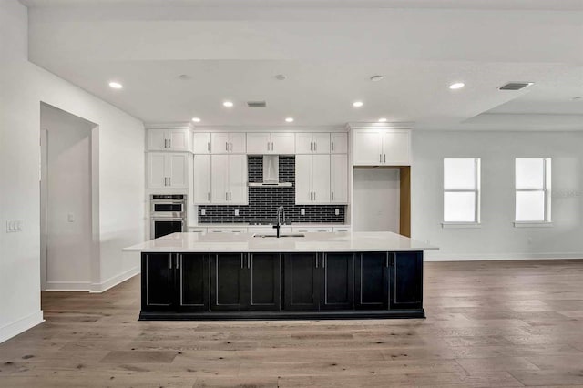 kitchen featuring light hardwood / wood-style floors, a spacious island, wall chimney range hood, and white cabinetry