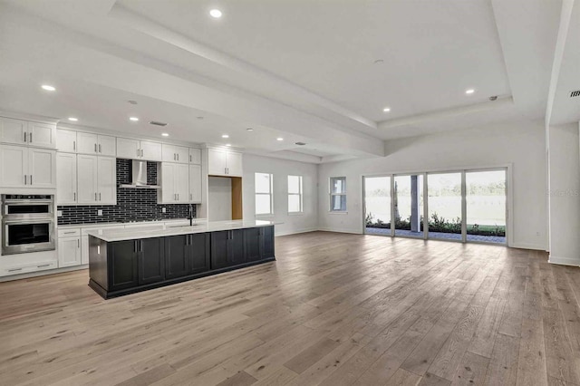 kitchen with white cabinets, a center island with sink, and light hardwood / wood-style flooring