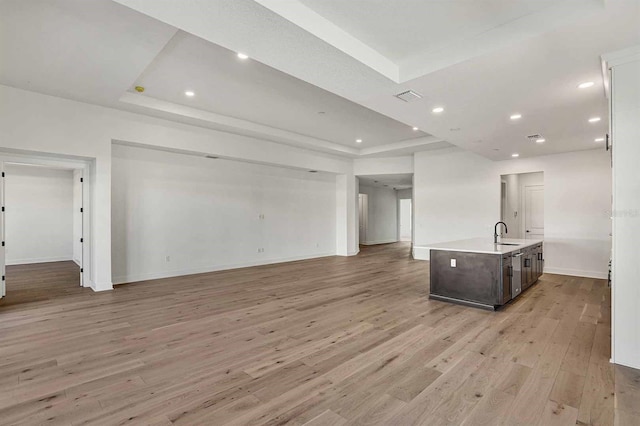 unfurnished living room with a raised ceiling, light hardwood / wood-style flooring, and sink