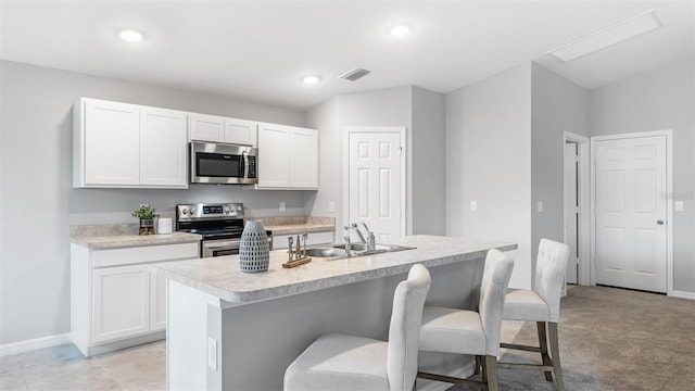 kitchen with a breakfast bar area, stainless steel appliances, a center island with sink, sink, and white cabinetry